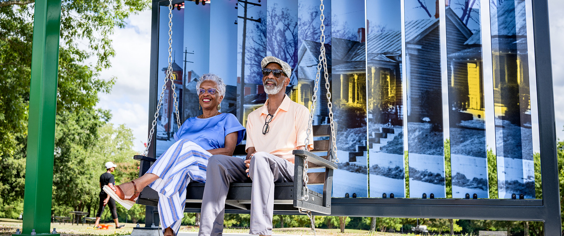 A couple sitting on a swing in front of Town Common artwork