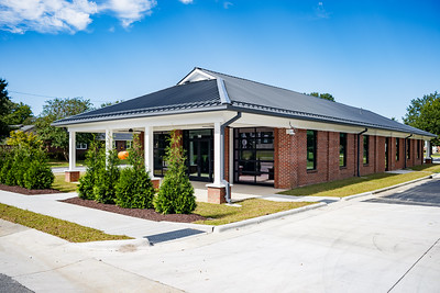 Outside photo of Dream Park Community Building with large windows at the front and some cedar trees in front