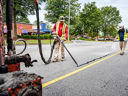 A man applying sealant to a crack in the road